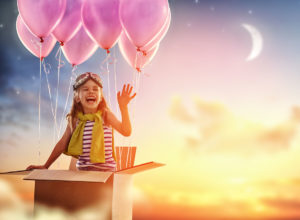 Enfant qui rit dans un carton qui s'envole emporté par des ballons.